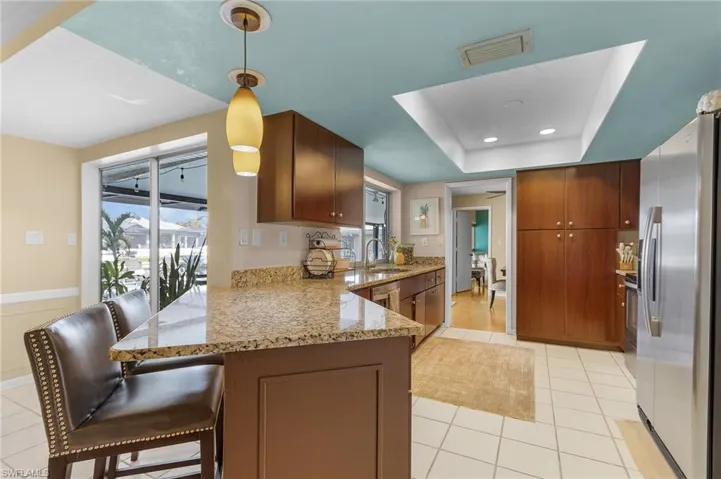 Kitchen with sink, kitchen peninsula, hanging light fixtures, a kitchen breakfast bar, and stainless steel refrigerator with ice dispenser