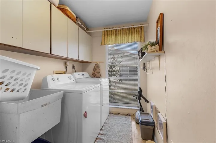 Laundry room featuring sink, washing machine and dryer, light tile patterned floors, and cabinets