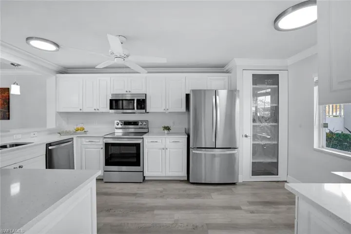 Spacious kitchen featuring appliances with stainless steel finishes, Coretex vinyl flooring, decorative glass pantry door, and white cabinetry