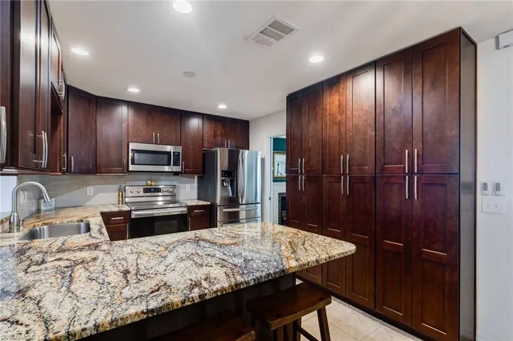Kitchen with stainless steel appliances, light stone counters, backsplash, a peninsula, and a kitchen bar