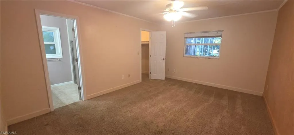 primary bedroom with ornamental molding, a spacious closet, light colored carpet, ceiling fan, and ensuite bathroom