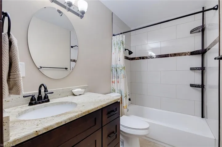 Guest Bathroom with shower / bathtub combination with curtain, vanity, and light tile patterned floors