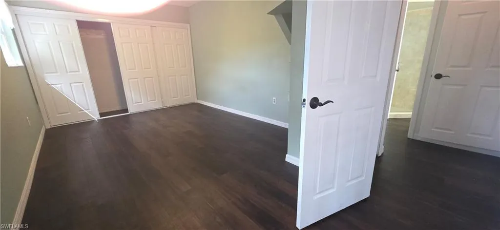 Unfurnished bedroom with dark wood-style floors and a closet