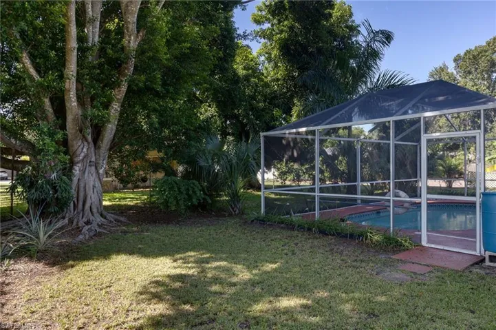 View of grassy yard featuring an outdoor pool, a lanai, and mature shade trees