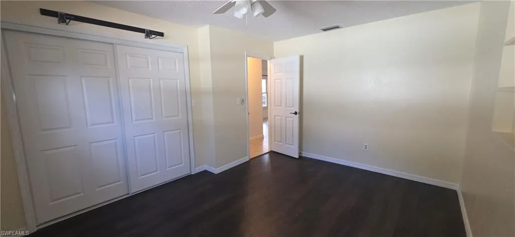 Unfurnished bedroom with dark wood-type flooring, a closet, a ceiling fan, and a textured ceiling