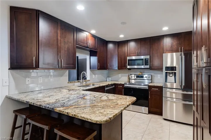 Kitchen featuring appliances with stainless steel finishes, a kitchen breakfast bar, dark brown cabinetry, a peninsula, and light stone counters