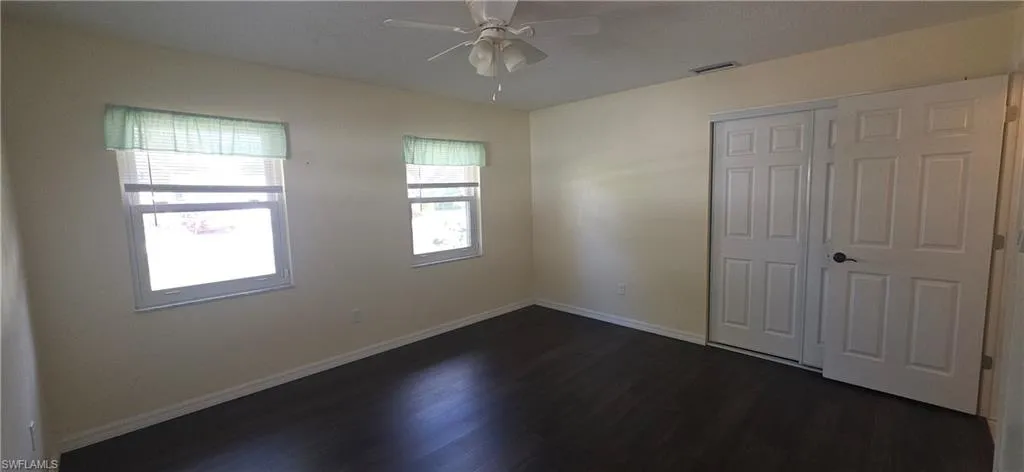 Unfurnished bedroom featuring dark wood-type flooring, a closet, and a ceiling fan