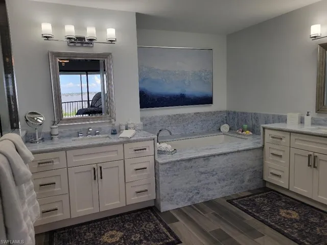 Full bath with two vanities, a garden tub, and dark wood-style floors