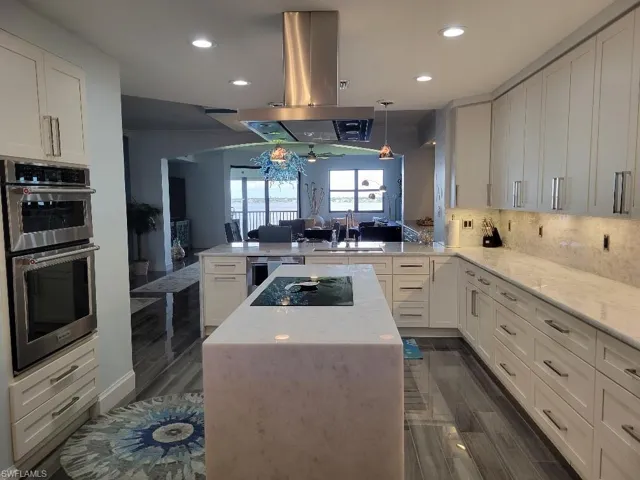 Kitchen with white cabinets, decorative backsplash, a peninsula, a kitchen island, and light stone counters