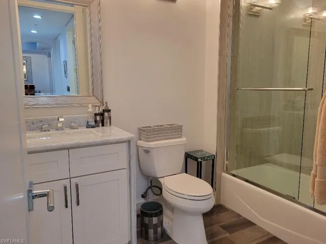 Full bathroom with vanity, dark wood-style floors, and enclosed tub / shower combo