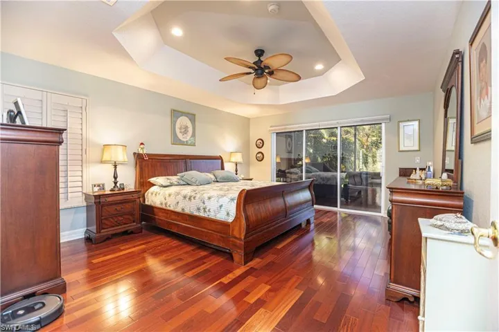 Bedroom featuring wood-type flooring, access to exterior, ceiling fan, a tray ceiling, and recessed lighting