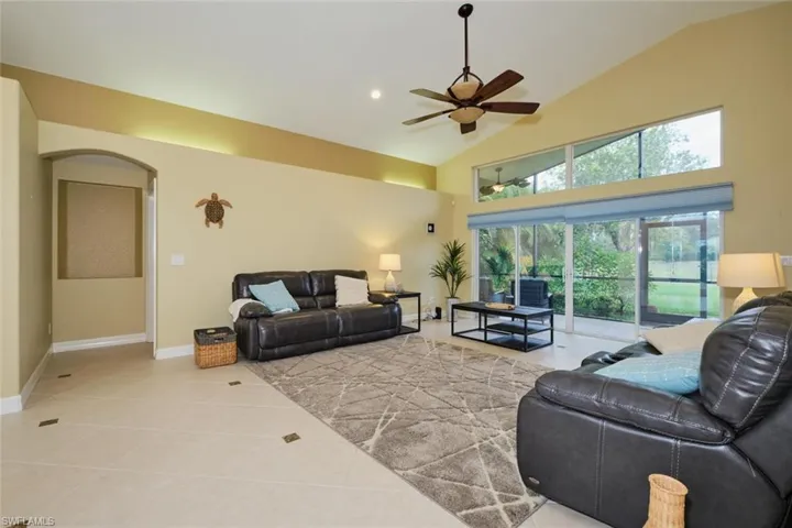 Living area featuring light tile patterned floors, vaulted ceiling, arched walkways, a ceiling fan, and recessed lighting