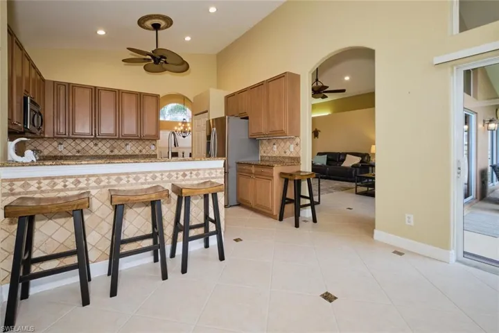 Kitchen featuring a kitchen breakfast bar, ceiling fan, backsplash, arched walkways, and a peninsula
