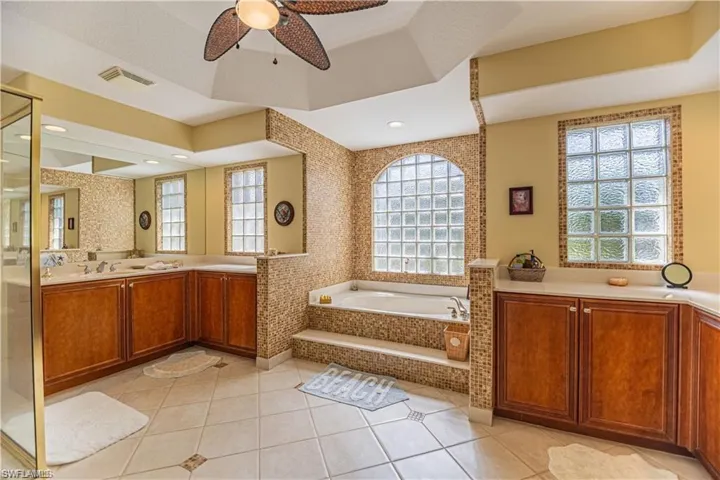 Full bath with two vanities, a garden tub, light tile patterned floors, ceiling fan, and a stall shower