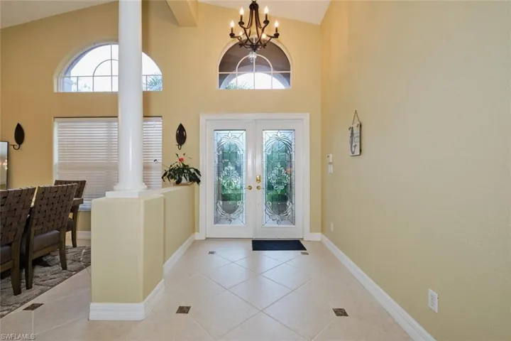 Entryway with hanging lights, french doors, plenty of natural light, light tile patterned floors, and a high ceiling