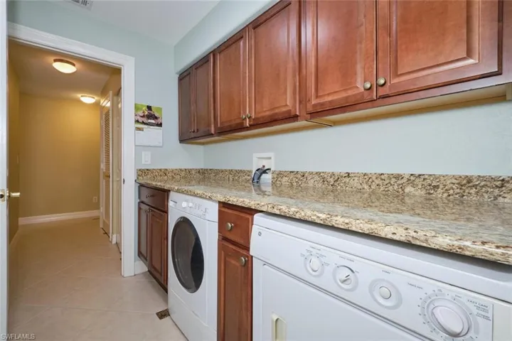 Laundry area with light tile patterned flooring, independent washer and dryer, and cabinet space