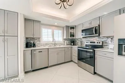 Kitchen featuring gray cabinets, stainless steel appliances, a raised ceiling, light countertops, and crown molding