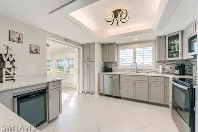 Kitchen featuring a tray ceiling, gray cabinetry, stainless steel appliances, backsplash, and light tile patterned floors