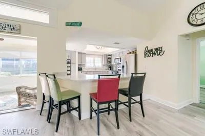 Kitchen featuring a breakfast bar, a peninsula, light wood-style flooring, light countertops, and stainless steel fridge with ice dispenser