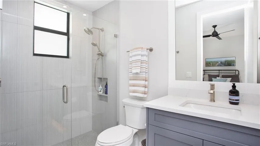 Bathroom featuring vanity, ceiling fan, toilet, and a shower with shower door