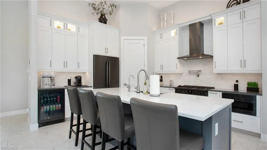 Kitchen featuring white cabinets, wall chimney range hood, a center island with sink, and appliances with stainless steel finishes