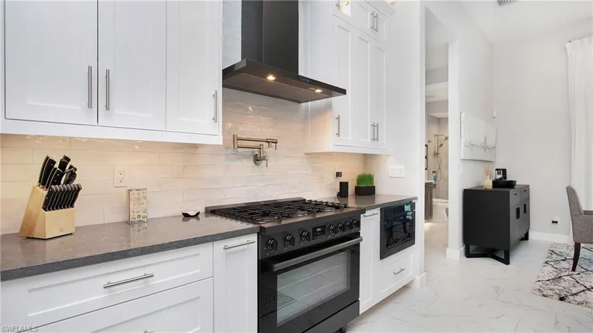 Kitchen with range with gas cooktop, wall chimney exhaust hood, and white cabinets