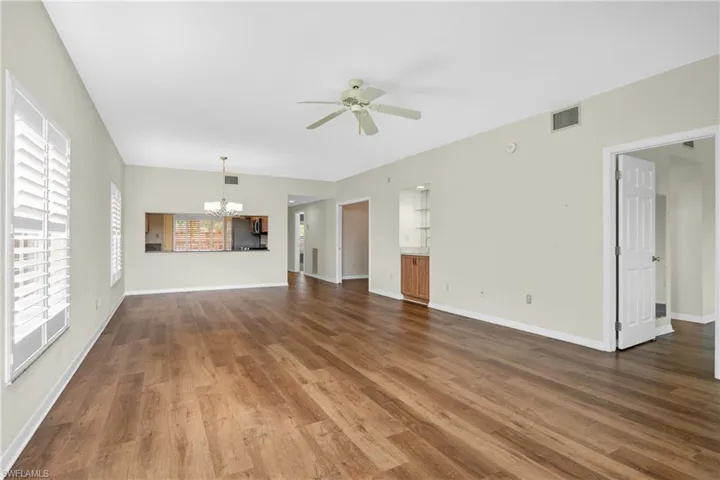 Unfurnished living room with baseboards, visible vents, ceiling fan with notable chandelier, and wood finished floors
