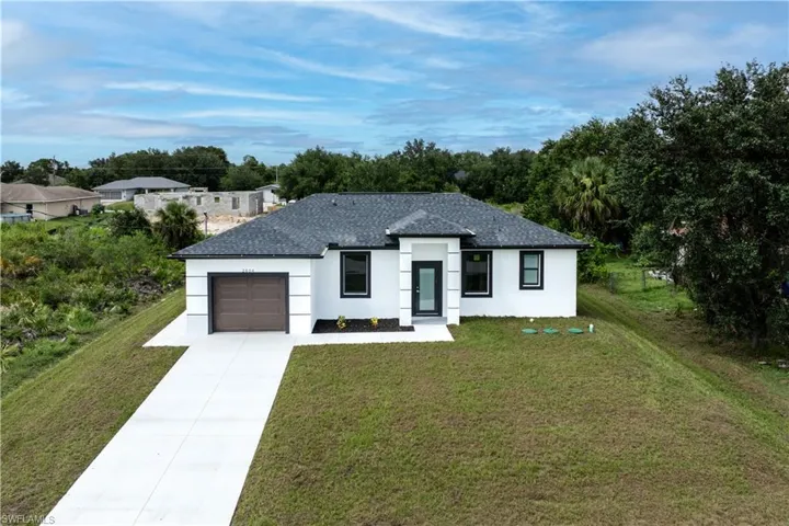 Modern farmhouse featuring stucco siding, driveway, a front yard, a garage, and a shingled roof