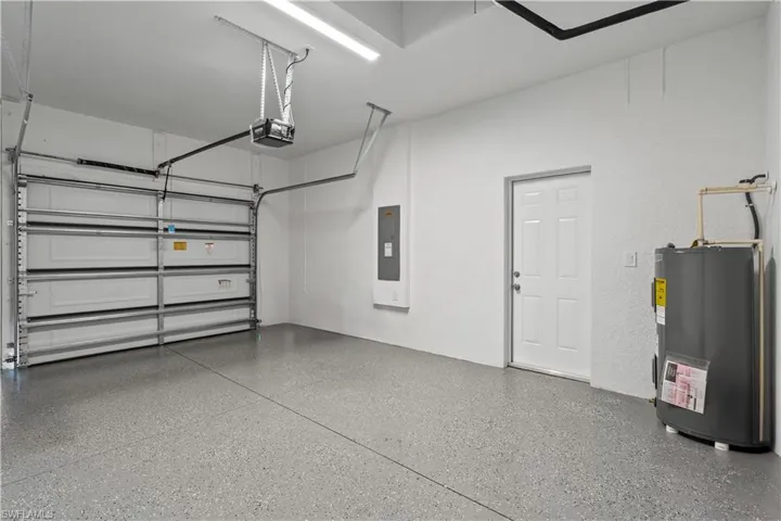 Garage with water heater, electric panel, and a garage door opener