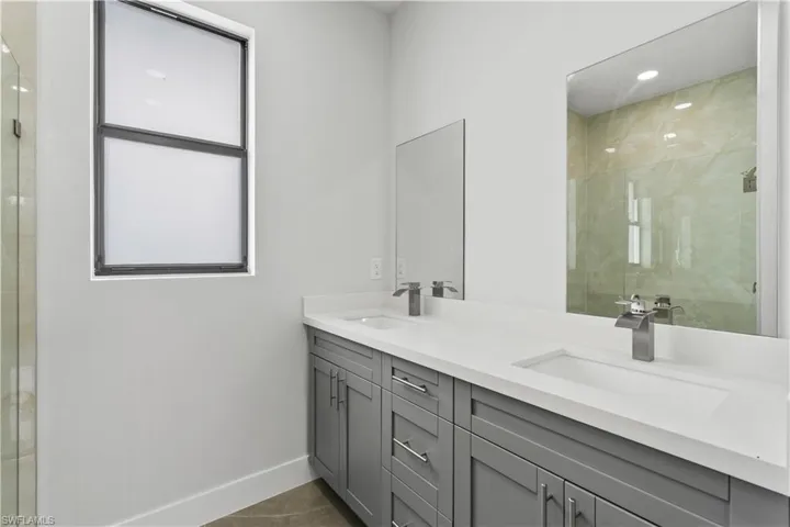 Full bathroom with double vanity, a shower stall, and dark tile patterned floors