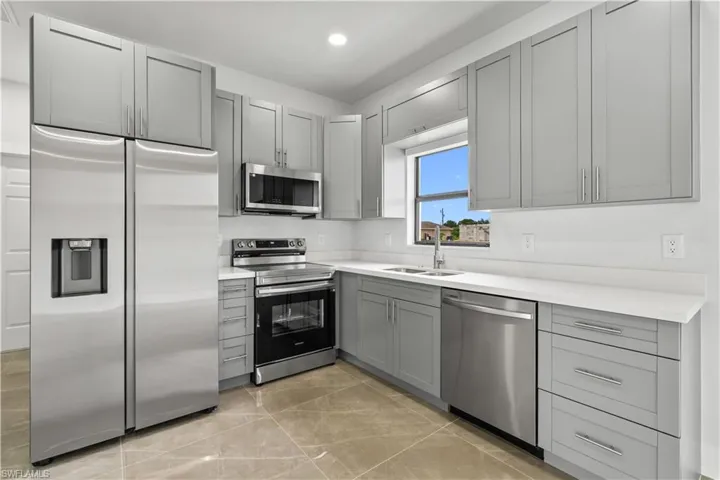 Kitchen with appliances with stainless steel finishes, gray cabinetry, recessed lighting, light tile patterned floors, and light stone counters