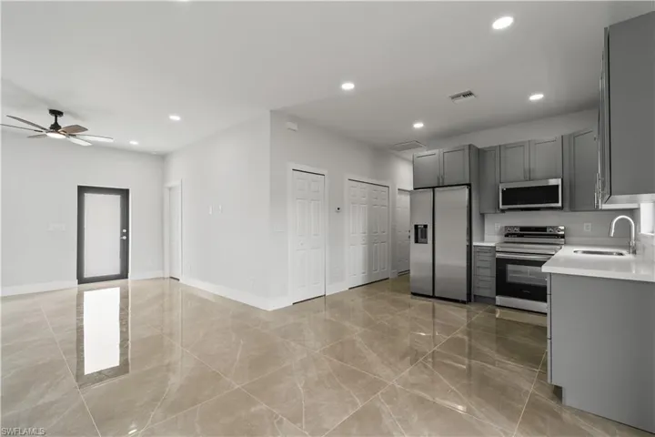 Kitchen with appliances with stainless steel finishes, recessed lighting, gray cabinets, open floor plan, and light stone counters