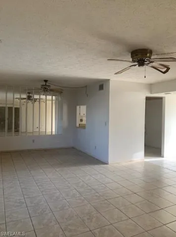 Unfurnished room featuring a textured ceiling, light tile patterned floors, and ceiling fan