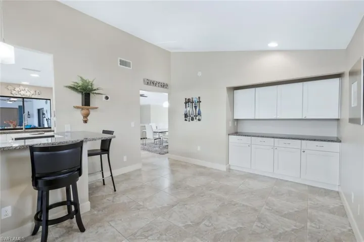 Kitchen featuring vaulted ceiling, white cabinetry, dark stone counters, and a breakfast bar area