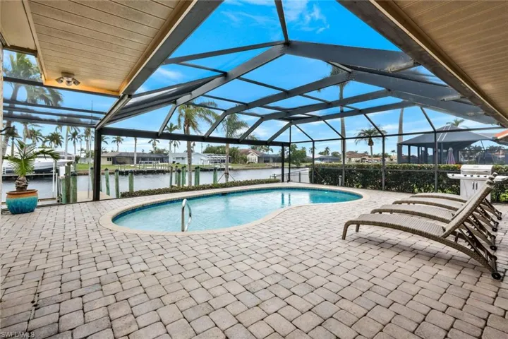 View of swimming pool featuring glass enclosure, a boat dock, grilling area, a water view, and a patio