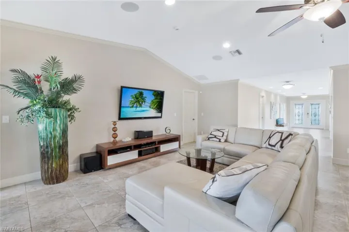 Living room with ceiling fan, lofted ceiling, crown molding, and french doors