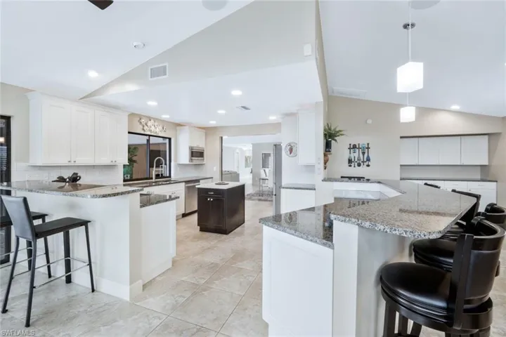 Kitchen featuring kitchen peninsula, white cabinetry, stainless steel appliances, and vaulted ceiling