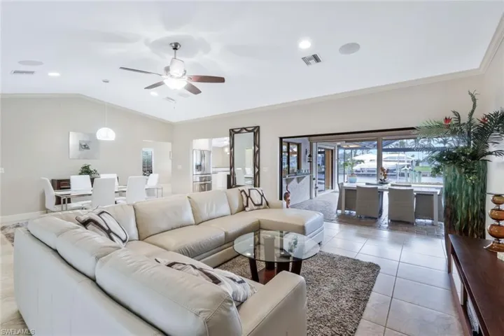 Tiled living room featuring ceiling fan, lofted ceiling, and ornamental molding