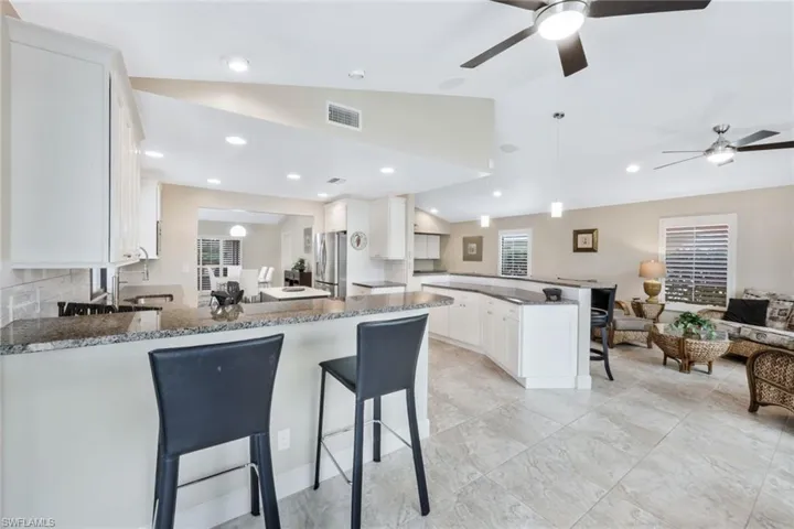Kitchen featuring kitchen peninsula, dark stone counters, a breakfast bar, white cabinetry, and lofted ceiling