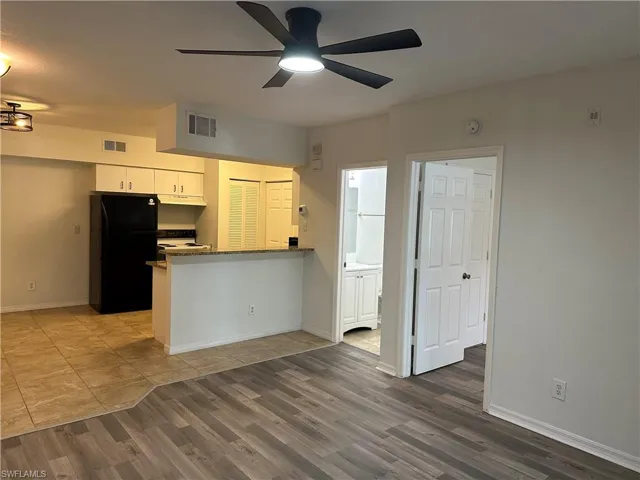 Kitchen featuring wood-type flooring, kitchen peninsula, black refrigerator, ceiling fan, and white cabinets