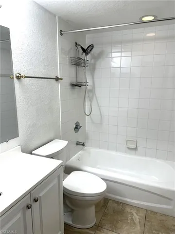 Full bathroom with tile patterned floors, toilet, tiled shower / bath combo, vanity, and a textured ceiling