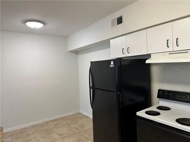Kitchen with white cabinets, white range with electric stovetop, light tile patterned flooring, and black fridge