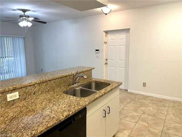 Kitchen featuring light tile patterned floors, sink, white cabinetry, ceiling fan, and dark stone counters