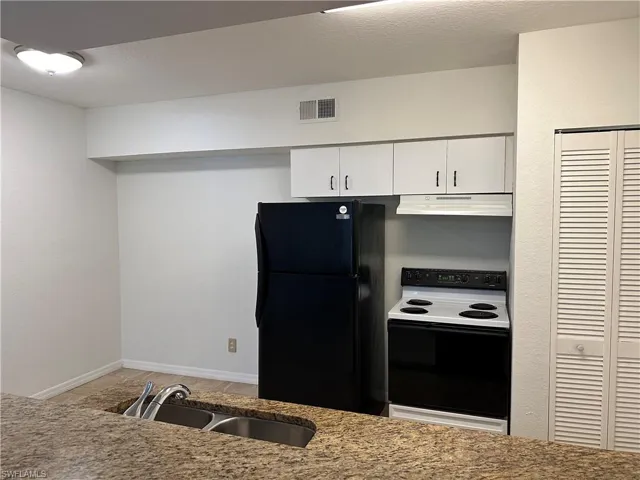 Kitchen featuring black fridge, white range with electric stovetop, white cabinetry, and sink