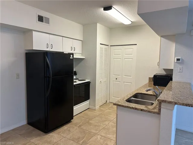 Kitchen with white cabinets, electric range, sink, black refrigerator, and a textured ceiling