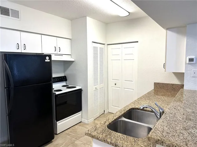 Kitchen featuring electric stove, black refrigerator, light tile patterned flooring, sink, and white cabinets