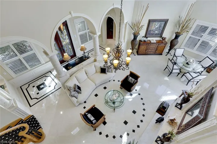 Living room with marble Floors and unique patterns, Marble posts, a towering ceiling approx. 25 ft, ornamental molding, and an inviting chandelier.  French doors to the pool and private beach, double sided stone fireplace that has never been used.