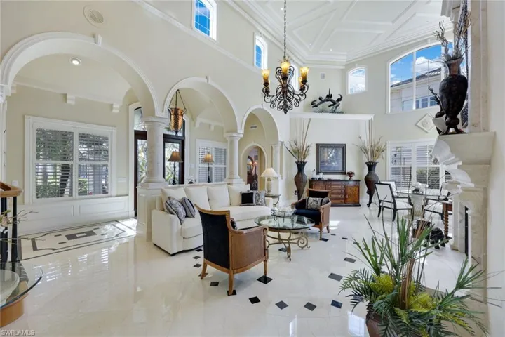 Living room with marble Floors, Marble posts, a towering ceiling approx. 25 ft, ornamental molding, and an inviting chandelier.  French doors to the pool and private beach, double sided fireplace that has never been used