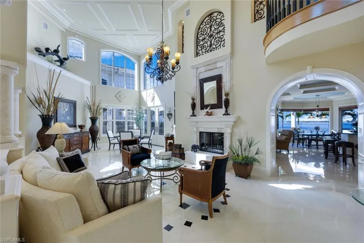 Living room with marble Floors, Marble posts, a towering ceiling approx. 25 ft, ornamental molding, and an inviting chandelier.  French doors to the pool and private beach, double sided fireplace that has never been used