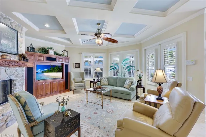 Living room featuring 2 sets of French doors, coffered ceiling, ceiling fan, ornamental molding, the 2nd side of the 2 sided fireplace with hand painted stone.